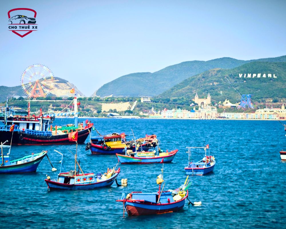 Một nhóm thuyền đánh cá đa sắc màu đang thả neo trên vịnh Nha Trang xanh ngắt, phía sau là đảo Hòn Tre