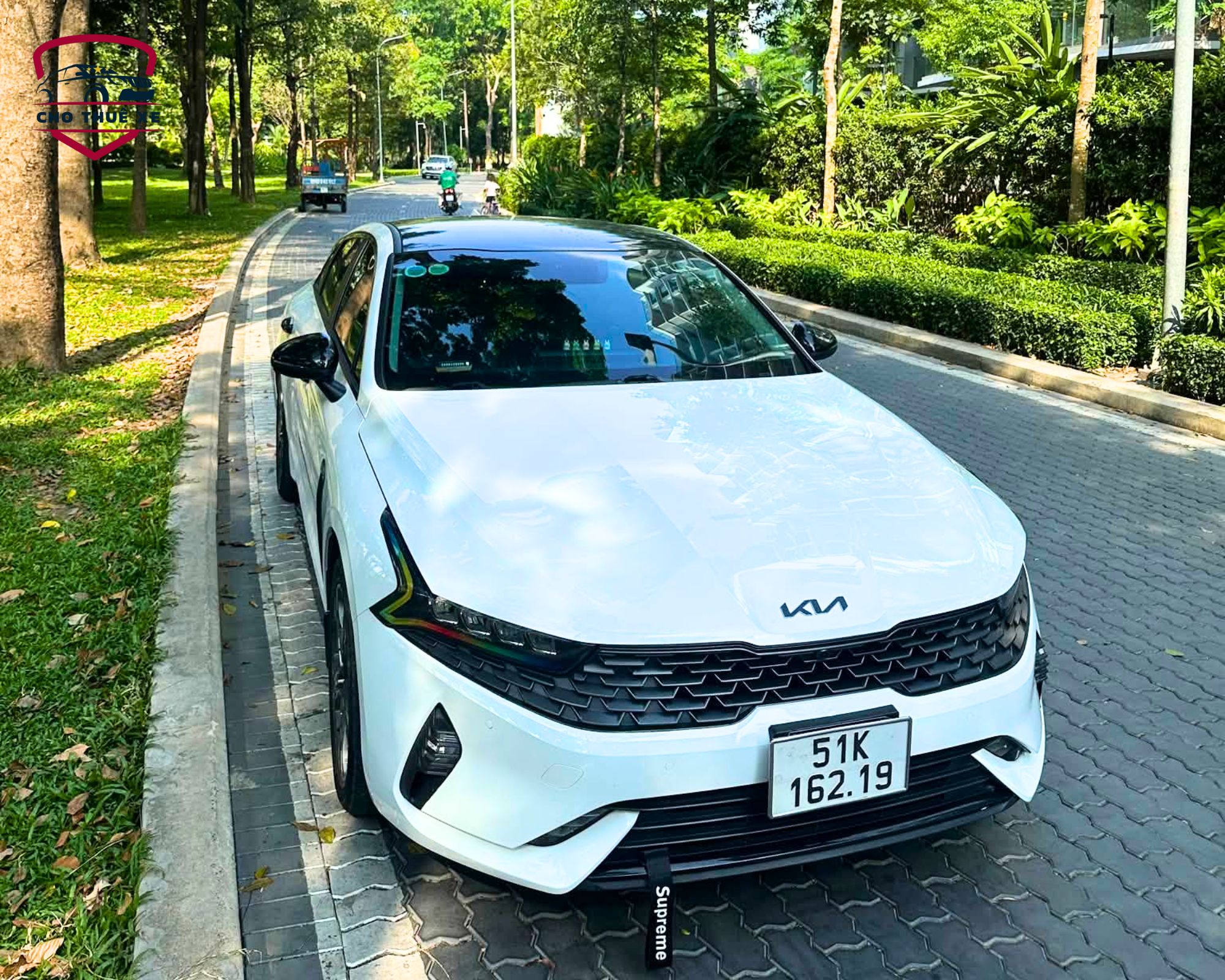 Xe Kia sedan 4 chỗ màu trắng nóc đen đỗ trên đường phố rợp bóng cây xanh