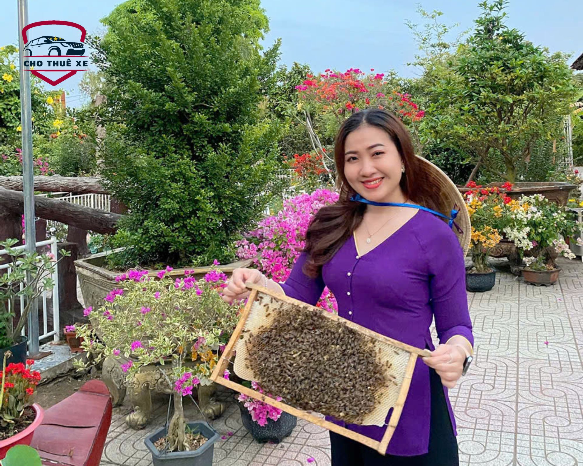 Người phụ nữ với nụ cười tươi tắn, mái tóc dài đen nhánh và chiếc nón lá truyền thống, tạo dáng bên khung mật ong
