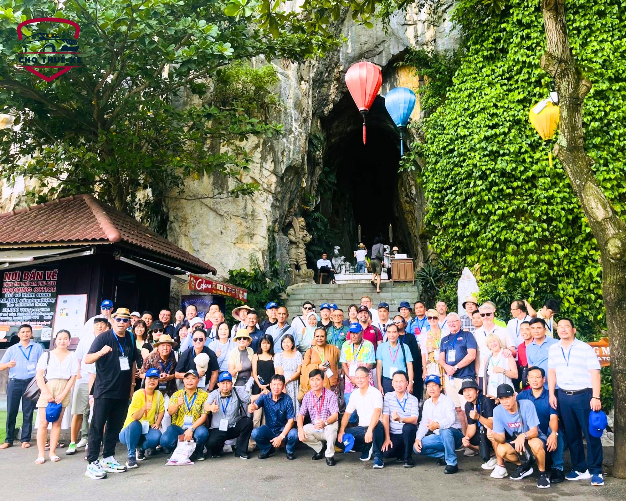 Bức ảnh nhóm đông người, một số đang ngồi và một số đang đứng, chụp trước Ngũ Hành Sơn với khung cảnh tự nhiên hùng vĩ và kiến trúc cổ kính