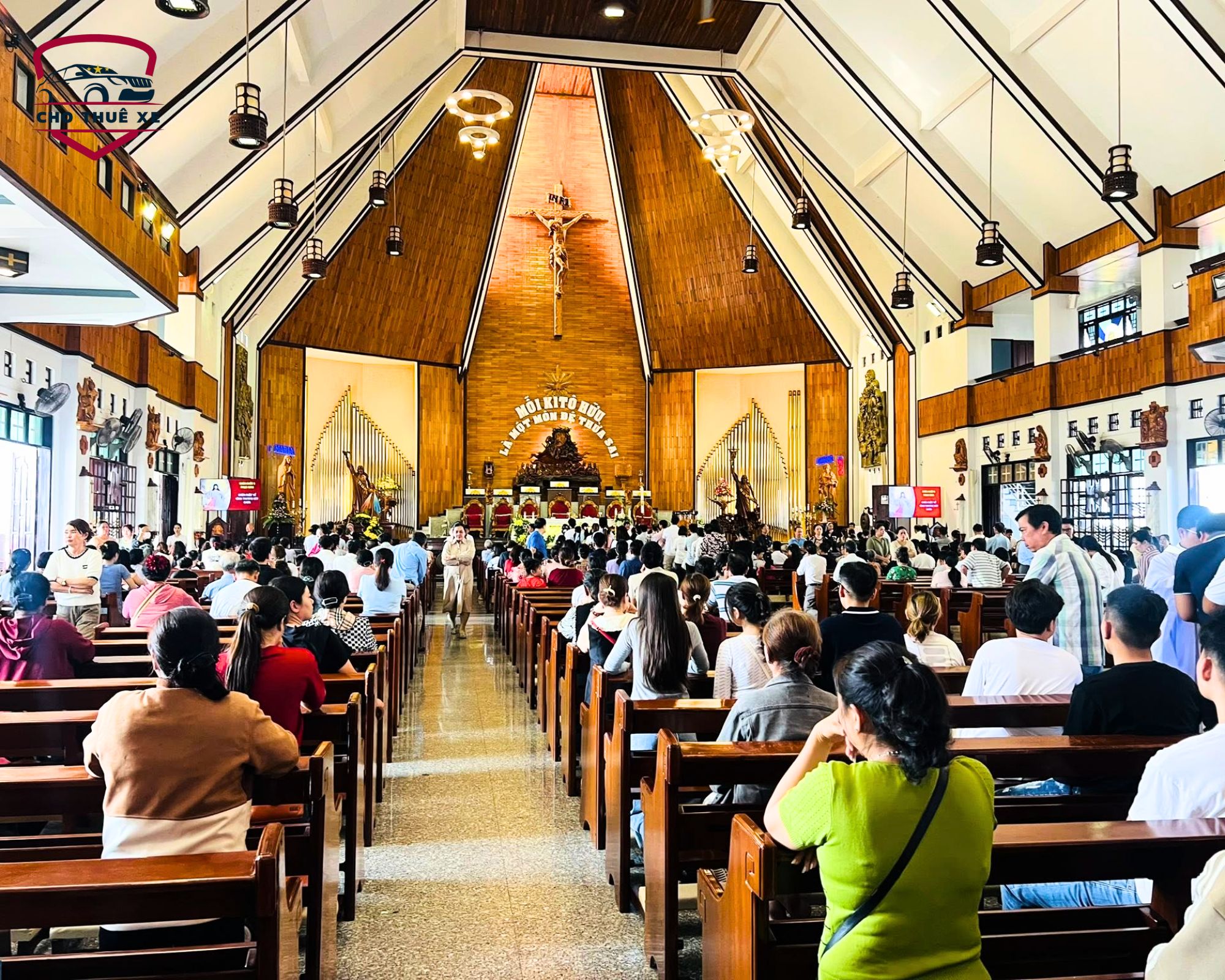 Khách hành hương và tín hữu ngồi kín các hàng ghế gỗ bên trong Thánh đường Tắc Sậy Bạc Liêu để cầu nguyện